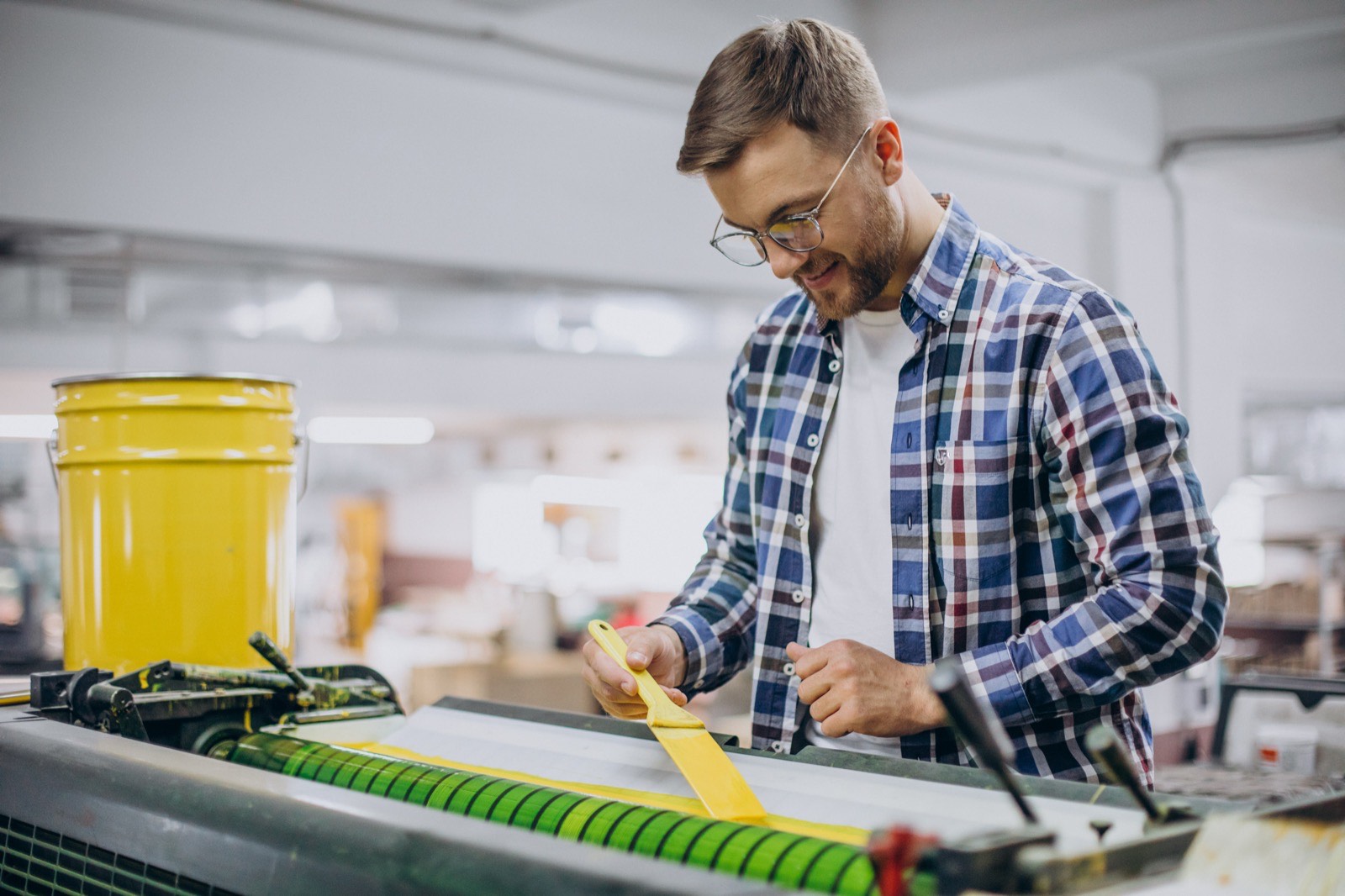 Print shop worker preparing a press with a yellow ink tool
