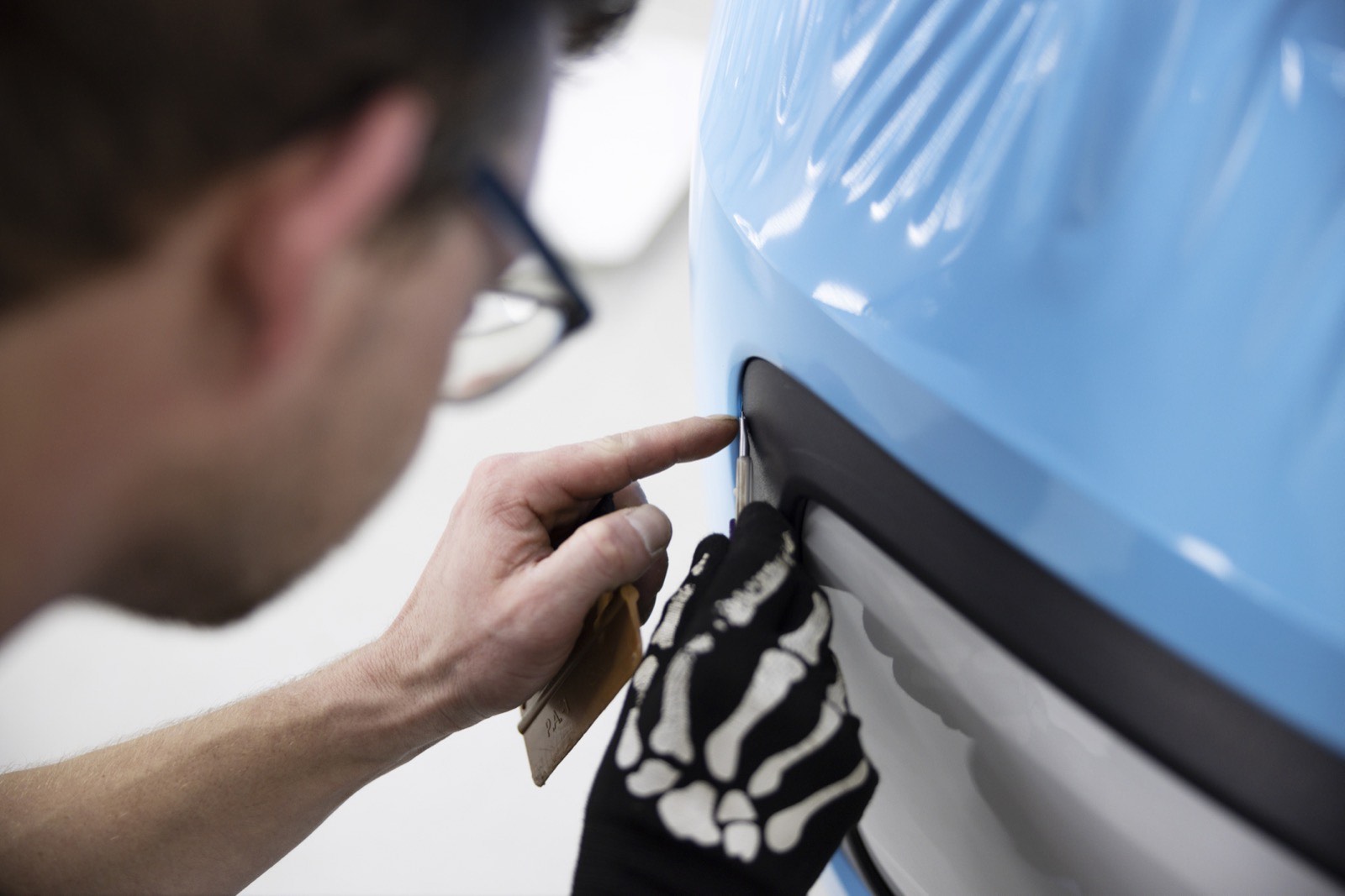 Wrap installer trimming blue vinyl beside a vehicle wheel arch